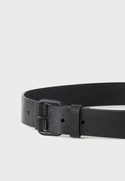 Ceinture en cuir noir avec boucle métallique rectangulaire noire mate et deux trous de réglage sur un fond clair uni.