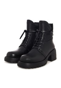 Par de botas de tobillo negras de cuero con cordones, con tacones gruesos y suelas de goma texturizada, mostradas sobre fondo blanco.
