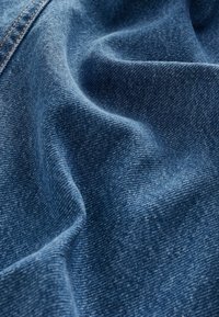 Tume sinine denimpind, millel on peen tekstuur, pehmed ja voolavad voldid ning nähtav kudumise muster. Heledast kontrastsetest lõngadest õmblused.