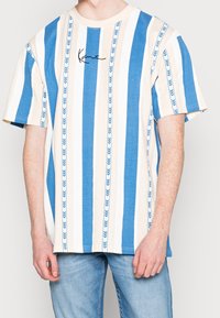 Blå och krämfärgad randig t-shirt med kort ärm, dekorerad med växtmotiv och en svart logotyp på bröstet. Tillverkad av mjukt bomullsmaterial.