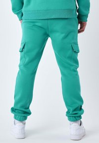 Turkise sweatpants lavet af en blanding af bomuld, med sidelommer, elastiske manchetter og en afslappet pasform. Parret med hvide sneakers.
