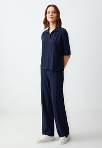 Dunkelblaues Strickset mit einem kurzärmligen Poloshirt mit strukturierten Mustern und weiten Hosen, kombiniert mit weißen Sneakern.