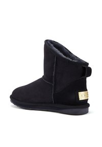 Zwarte suede enkellaarsjes met een zachte voering, een platte zool en een logo-plaat in goudkleur aan de zijkant. Stiknaaddetails zijn zichtbaar.