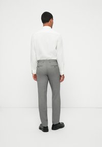 Harmaat räätälöidyt housut, joissa on takataskut, yhdistettyinä valkoiseen paitaan. Housuissa on sileä pinta ja slim fit -malleja. Mustat kengät viimeistelevät asun.