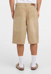 Beige knielange shorts van katoen, met twee achterzakken, net gestikte naden en een soepele textuur. Bruin leren accent op de tailleband.