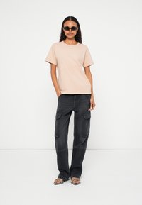 Gaiši rozā kokvilnas T-krekls ar īsām piedurknēm un apaļu kakla izgriezumu, kopā ar melnām kargo biksēm ar sānu kabatām un brīvu piegriezumu.