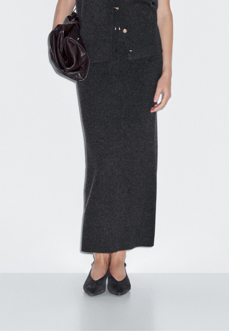 Robe en tricot gris foncé avec un buste boutonné, jupe longueur cheville, associée à des ballerines noires et un sac marron foncé. Texture lisse, design minimal.
