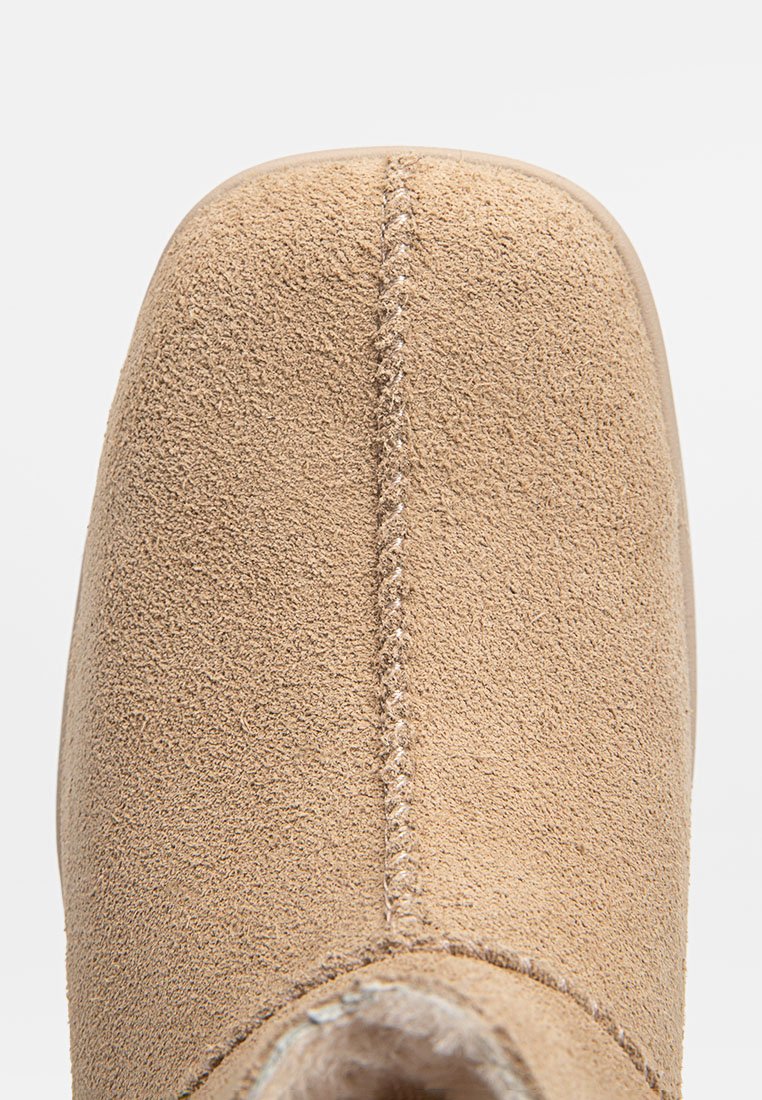 Acercamiento a la punta de una bota de ante beige con costura central y superficie suave y texturizada.