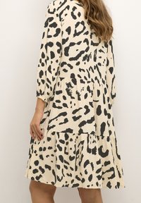 Kremowa sukienka w czarno-abstrakcyjny wzór zwierzęcy, z rękawami o długości trzy czwarte, warstwową spódnicą i luźnym krojem. Gładka tekstura materiału.
