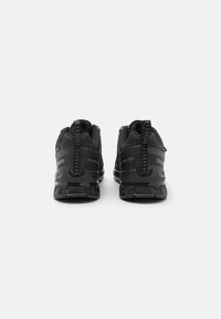 Black athletic shoes with textured mesh upper, reinforced heel, and rubber sole. Features pull-tabs and branding on heel and side.