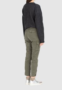 Tmavě šedý krátký svetr s texturovaným úpletem, doplněný olivově zelenými nákladními kalhotami s bočními kapsami a teniskami se stříbrnými detaily.