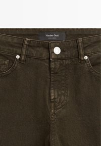 Jean en denim vert olive foncé avec une étiquette, un bouton en métal argenté, et un design classique à cinq poches avec des détails de couture visibles.