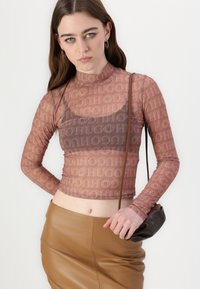 Dlouhý rukáv, průhledný, upnutý top v barvě dusty rose s opakujícím se logem "HUGO"; kombinovaný s hnědou koženou tužkovou sukní a malou černou kabelkou.