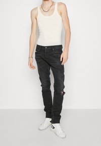 Svarta denimjeans med slitet utseende, bärs med en figurnära vit linne och vita sneakers med blå accenter.