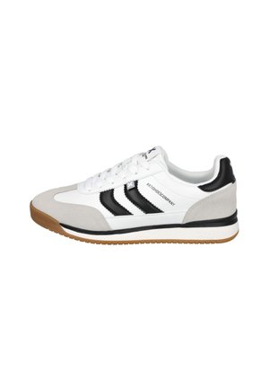 Zapatilla blanca con puntera de ante beige, rayas negras a los lados, cordones blancos y suela de goma, vista desde el lado exterior.