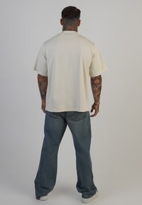Beige bomulds t-shirt med korte ærmer, parret med løstsiddende blå denim jeans. T-shirten har en lige pasform og minimal detaljering.