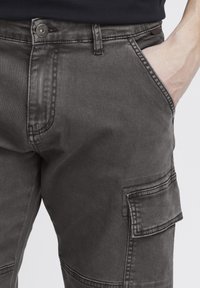 Gray denim cargo pants featuring front pockets, a button closure, and side cargo pocket, with a slightly worn texture.