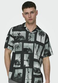 Camisa de manga corta con estampado en blanco y negro que presenta diversas imágenes de playa y surf en un patrón de cuadrícula, con un cuello abotonado.
