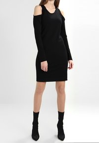 Svart klänning med långa ärmar och utskärningar på axlarna. Slim fit, stretchigt tyg, knä-lång, kombinerad med svarta sockboots.