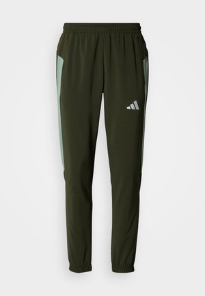 Pantalones deportivos color verde oliva con paneles laterales en verde claro, cintura elástica, dos bolsillos laterales y un logo reflectante en el muslo izquierdo.