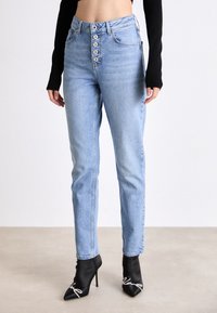 Ljusblå hökvalitetsjeans med femknappsframslutning, rak benform och subtila blekningar. Bärs med svarta högklackade stövlar.