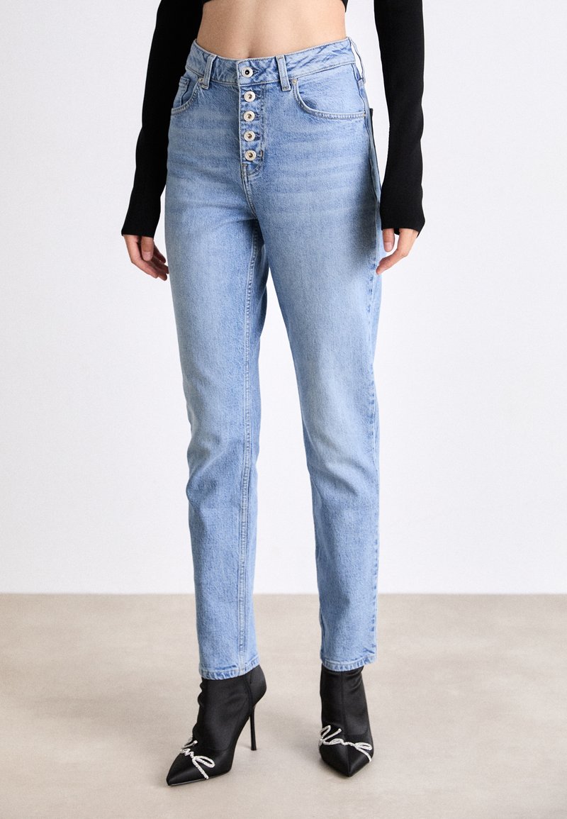 Ljusblå hökvalitetsjeans med femknappsframslutning, rak benform och subtila blekningar. Bärs med svarta högklackade stövlar.