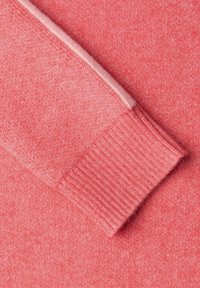 Pletený svetr v živé světle růžové barvě s žebrovaným detailem na manžetách. Látka má hladkou, měkkou texturu bez vzorů.