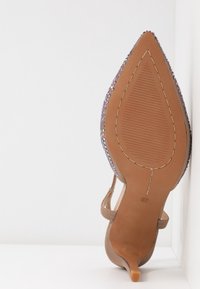 Chaussure pointue marron clair avec un talon aiguille. Présente des sequins le long du bord extérieur et une semelle en caoutchouc texturée.