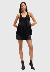 Black, sleeveless blouse with a layered design, featuring ruffled accents and a flowing silhouette. Worn over a black leather skirt and ankle boots.