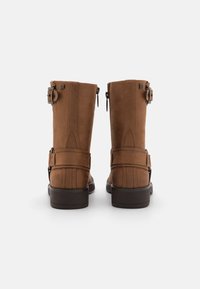 Botas de tobillo de ante marrón con un acabado texturizado, que cuentan con un cierre lateral de cremallera y detalles de hebilla ajustable en el tobillo exterior, además de un tacón ancho.