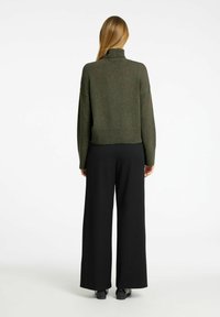 Olivgrüner Strick-Turtleneck-Pullover, kombiniert mit schwarzen, weit geschnittenen Hosen. Der Pullover hat einen gerippten Saum und ein Design mit überschnittenen Schultern.