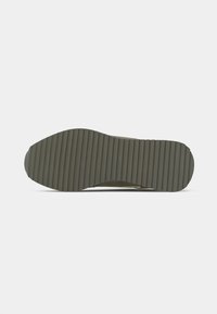 Rubber outsole with vertical ribbing pattern, featuring a rounded toe and neutral olive color. Durable material, designed for traction.