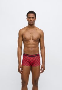 Κόκκινα ανδρικά εσώρουχα boxer με μαύρο ζωνάκι στη μέση, διακοσμημένα με επαναλαμβανόμενο λογότυπο σε αποχρώσεις του κόκκινου και μαύρου. Ομαλή υφή και εφαρμοστό σχέδιο.