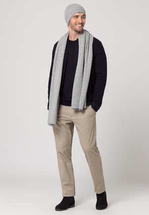 Grijze gebreide beanie en sjaal over een donkere trui; beige broek en zwarte enkellaarsjes. Casual, gelaagde outfit met zachte texturen.