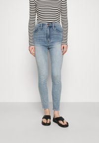 Světle modré džíny s vysokým pasem a úzkým střihem, které mají pět kapes a jemné opotřebení. Spárované s černobílým proužkovaným dlouhým rukávem.