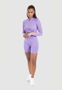 Lichtpaarse actieve kleding set met een korte, ritsbare top met lange mouwen en hoge taille shorts, gecombineerd met witte sneakers.