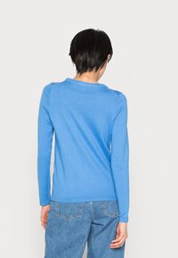 Maglione blu a maniche lunghe con scollo rotondo, texture a coste e silhouette aderente, abbinato a jeans blu chiaro.