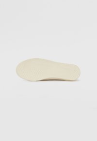 Suola della scarpa realizzata in gomma crema chiara con un motivo testurizzato e ondulato. Forma arrotondata con fondo piatto. Branding minimo visibile.