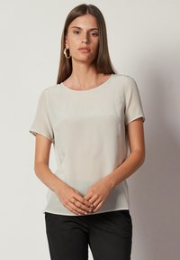 Ljusbeige kortärmad blus med rundad halsringning, mjuk textur och avslappnad passform. Matchas med mörka byxor för kontrast.