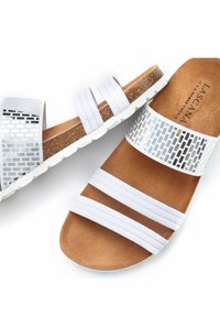 Witte schuimslippers met drie stoffen bandjes en metallic gemusterde accenten. Kurken voetbed en witte rubberen zool. Zachte textuur overal.