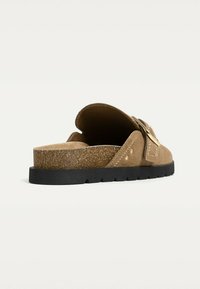Brown suede slide sandals with a cork base, featuring a wide strap and gold-colored hardware. The sole is black and textured for grip.