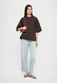 T-shirt oversize marrone, jeans a gamba larga blu chiaro con orlo sfrangiato, scarpe a strisce multicolori e una piccola borsa rossa.