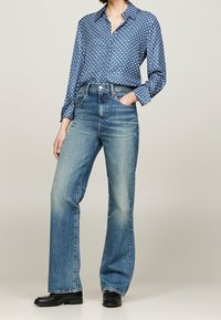 Sininen pilkullinen napitettava paita, pitkät hihat; vaaleansiniset suoralahkeiset farkut, taskut, yhdistetty mustiin nilkkabootseihin.