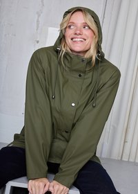 Alyvuogių žalios spalvos vandeniui atspari striukė su gobtuvu, priekyje spaudžiamais užsegimais, reguliuojamomis raišteliais ir lygia, glotnia tekstūra.