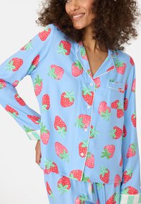 Baumwoll-Schlafanzugset mit hellblauem Hintergrund, großen roten Erdbeeren und grünen Blättern. Enthält ein kurzärmliges Hemd und eine Hose.