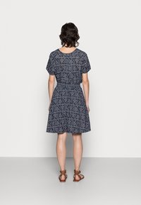 Laivansinen mekko, jossa on paisley-kuvio, lyhyet hihat, kapea vyötärö ja levenevä hame, valmistettu kevyestä kankaasta. Ruskeat remmissandaalit.