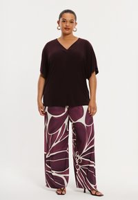 Bordeauxrotes V-Ausschnitt-Oberteil kombiniert mit weitem Hosenbein und großem Blumenmuster in Purpur- und Weißtönen. Glatter Stoff, lockere Passform.