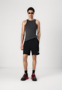 Szary prążkowany top na ramiączkach, czarne spodenki z logo, czarno-czerwone chunky sneakers i okulary przeciwsłoneczne. Prosty, sportowy strój.