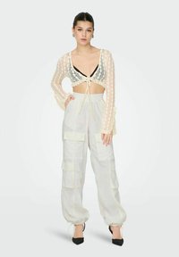 Läbikaga lõikelise Crop top, millel on ees lips, koos kergete, heledate taskupükstega, millel on taskud ja kogutud mansetid.