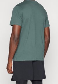 Koszulka z krótkim rękawem w stonowanym zielonym kolorze, wykonana z bawełny, z okrągłym dekoltem i gładką fakturą, w zestawieniu z ciemnymi szortami.